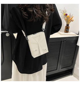 Detail of white tuxedo-style box bag with tie design worn as a crossbody bag