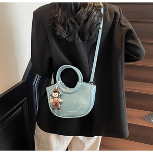 Close-up of a light blue semi-circular handbag with retro texture and a cute boy charm