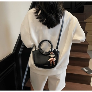 Detail of a black matte leather bucket bag with ring handle and a cute knit charm