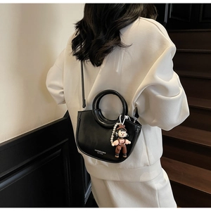 Detail of black semi-circular bucket bag with hollow handle and cartoon pendant on model