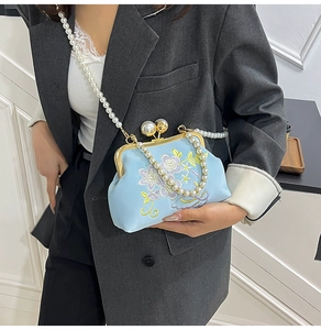 Detail of light blue floral embroidery and pearl clasp on a vintage crossbody bag