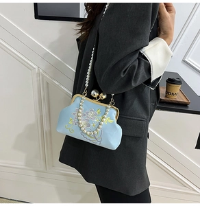 Detail of light blue evening bag with floral embroidery and large pearl clasp accents