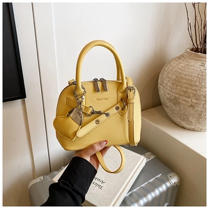 Detail of yellow shell bag featuring lychee grain leather, brand logo and heart charm