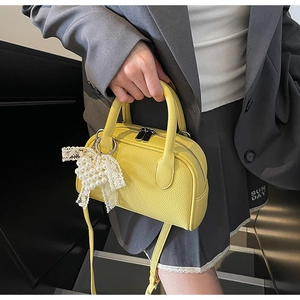 Dettaglio della mini borsa gialla in pelle con ciondolo a fiocco in pizzo e metallo argento