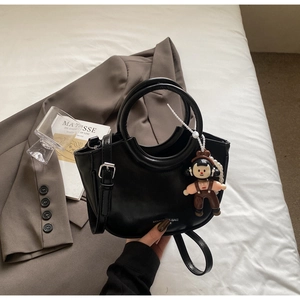 Detail of black matte leather bucket bag with top circular handle and cartoon doll charm