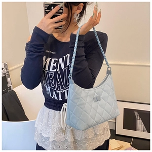 Detail of light blue quilted underarm bag with matching chain strap worn by a model