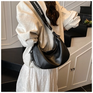 Détail du sac croissant en cuir noir avec bandoulière large en textile à logo