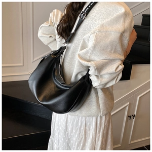 Détail d'un sac hobo en cuir grainé noir avec une large bandoulière en tissu imprimé