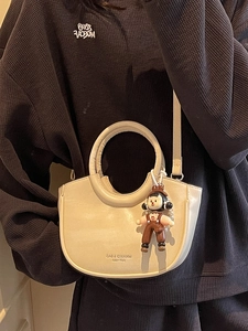 Chic beige bucket bag with circular cutout handle and cute doll charm for women
