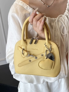 Modern yellow shell-shaped handbag with pebbled leather texture and heart charm
