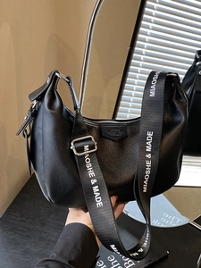 Sac hobo noir chic avec une large bandoulière lettrée et une finition en cuir grainé