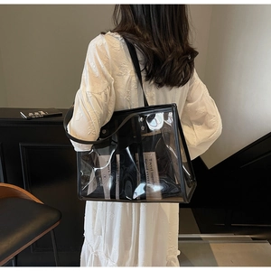 Rear view of a clear PVC tote bag with black trim worn over the shoulder by a model