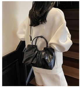 Detail of black pleated faux leather handbag showing glossy finish and slim shoulder strap