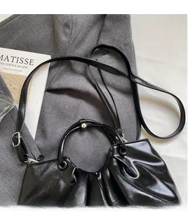 Detailed view of the shiny black pleated leather handbag with long shoulder strap