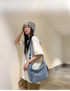 Détail du sac hobo en denim bleu avec large bandoulière porté par un mannequin en style