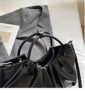Detail of black glossy pleated handbag with sturdy handles and premium leather texture