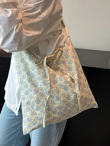 Floral tote bag with blue patterns, lace trim, and bow detail shown on a shoulder