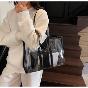 Detailed view of a transparent PVC tote bag with black trim worn by a model on a shoulder