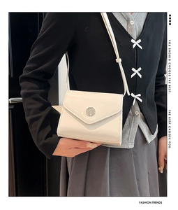 Détail d'un sac bandoulière en cuir verni crème brillant avec fermoir en métal rond