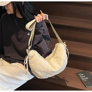 Minimalist beige nylon tote bag with drawstring detail shown on a model in a lifestyle setting