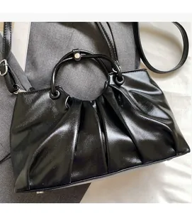 Close-up of black pleated tote bag featuring shiny finish and metal ring handle