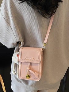 Pink patent leather crossbody phone bag with gold lettering and a soft fur pompom charm
