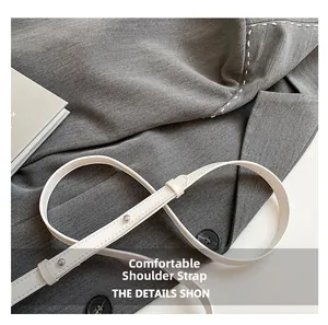 Détail d'une bandoulière en cuir blanc avec des clous argentés sur un blazer en tissu gris