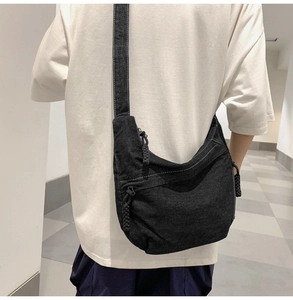 Detail of black denim crossbody bag with white stitching and braided zipper pulls