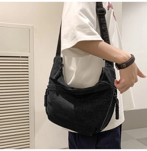 Detail of black denim crossbody bag featuring white contrast stitching and braided rope zipper
