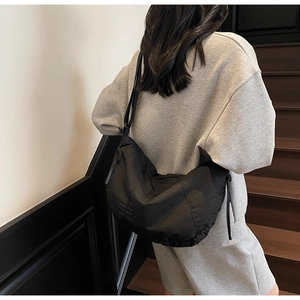 Rear view of a model wearing a large black nylon crescent tote bag on wooden stairs