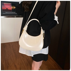 Detail of a creamy white crescent bag with gold metal buckles and adjustable strap