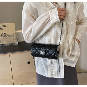 Détail d'un sac cylindre noir matelassé avec fermoir rotatif argenté et bandoulière chaîne