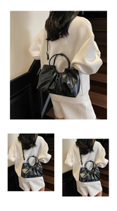 Detail view of black ruched handbag with glossy leather and round handles worn on stairs