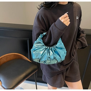 Metallic blue pleated crescent handbag displayed by model in a minimalist dark setting