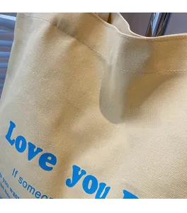 Close-up of beige canvas tote bag with vibrant blue 'Love you' letter printing