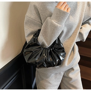 Detail of black pleated patent leather hobo bag showing glossy texture and craftsmanship