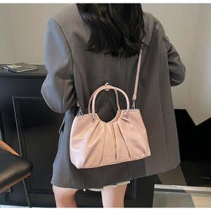 Detail of pink pleated handbag with metallic finish and unique arc handle worn by model