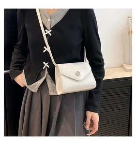 Détail d'un sac bandoulière en cuir verni blanc avec une boucle ronde en métal argenté