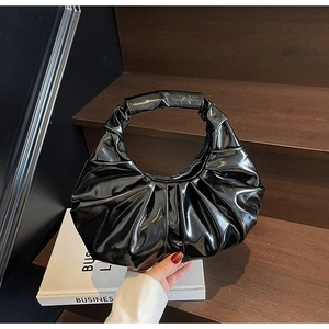 Detail of black glossy pleated handbag with minimalist handle on dark wooden background