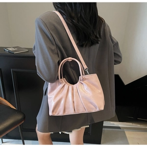Detail view of pink pleated leather handbag worn with a dark grey suit in a minimal setting