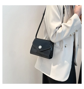 Détail d'un sac bandoulière en cuir verni noir avec boucle en métal argenté gaufré