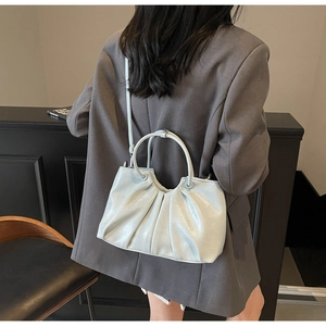 Detail view of light blue pleated handbag with metallic circular handle and shoulder strap