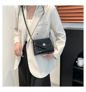 Gros plan du sac bandoulière en cuir verni noir avec boucle argentée sur un mannequin