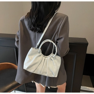 Model wearing a light beige ruched handbag with round handles and a detachable shoulder strap