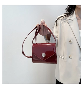 Détail d'un sac bandoulière en cuir verni bordeaux avec boucle métallique argentée gravée