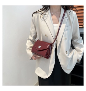 Détail d'un mini sac bandoulière en cuir verni bordeaux avec boucle argentée sur blazer blanc