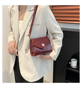 Détail du sac bandoulière en cuir verni bordeaux avec boucle argentée sur le mannequin