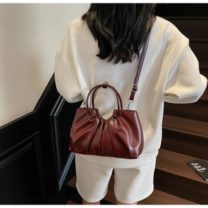 Detail view of burgundy ruched faux leather handbag with adjustable crossbody strap and handle