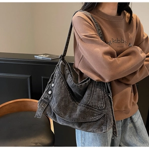 Detail of grey denim tote bag showing faded wash texture and metal buckle on wide strap
