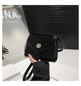 Détail du sac bandoulière en cuir verni noir avec logo rond en métal argenté brillant